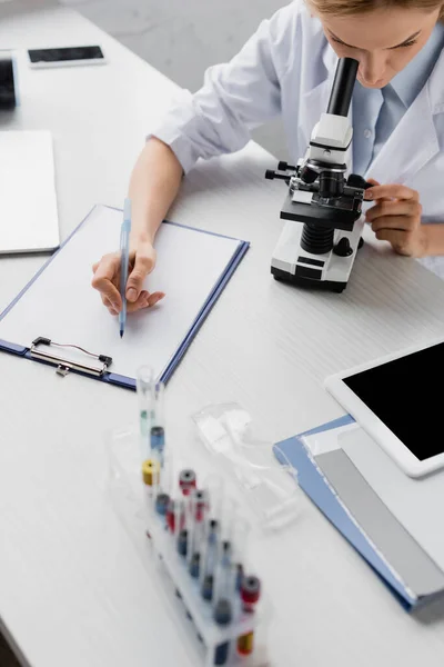Scientist holding pen while looking through microscope in lab — Stock Photo