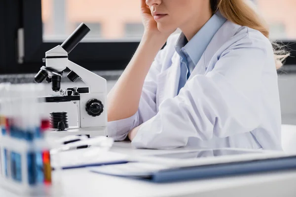 Cropped view of scientist leaning on hand near microscope in lab — Stock Photo