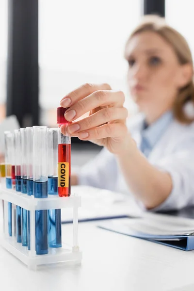 Test tube with sample and covid lettering in hand of nurse on blurred background — Stock Photo