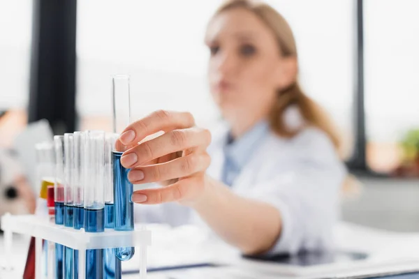 Reagenzglas mit verschwommener Flüssigkeit in der Hand des Wissenschaftlers auf verschwommenem Hintergrund — Stockfoto