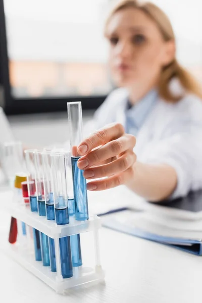 Reagenzglas mit verschwommener Flüssigkeit in der Hand des Arztes auf verschwommenem Hintergrund — Stockfoto