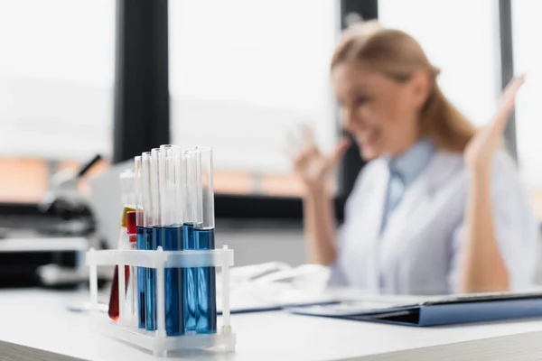 Test tubes with samples near cheerful scientist on blurred background — Stock Photo
