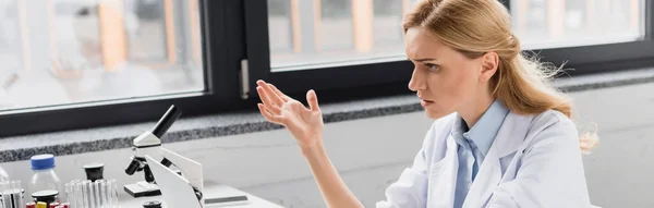 Científico disgustado gesto cerca del microscopio en el laboratorio, bandera — Stock Photo