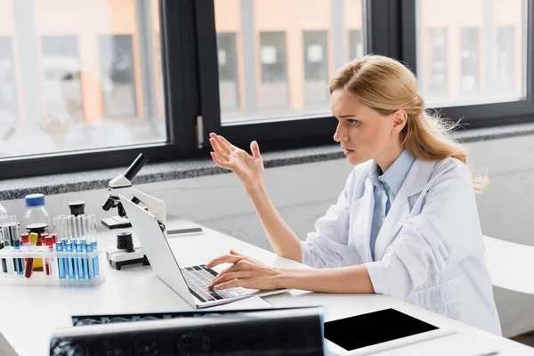 Unzufriedener Wissenschaftler gestikuliert neben Laptop und Mikroskop im Labor — Stockfoto