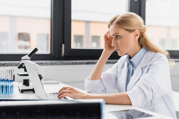 Scienziato premuroso che guarda il portatile vicino al microscopio in laboratorio — Foto stock