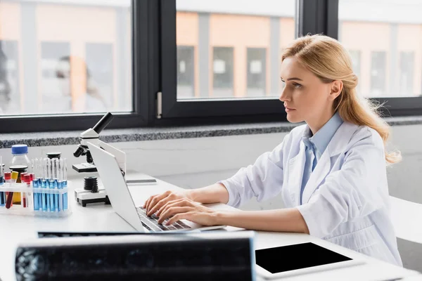 Scientist using laptop near microscope and devices in lab — Stock Photo