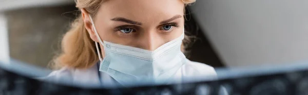 Ученый в медицинской маске глядя на рентген на размытом переднем плане, баннер — стоковое фото