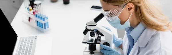 Scientist in medical mask looking through microscope on desk, banner — Stock Photo