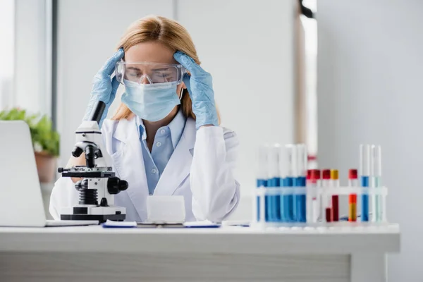 Cientista cansado em máscara médica e óculos com dor de cabeça em laboratório — Fotografia de Stock