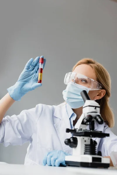 Scientist in medical mask and goggles holding test tube with covid lettering in laboratory — Stock Photo