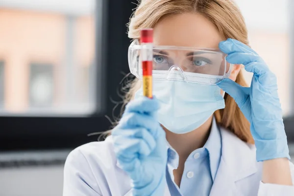 Scientist in goggles, latex gloves and medical mask holding test tube with covid lettering — Stock Photo