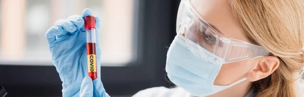 Cientista em máscara médica e óculos olhando para tubo de ensaio com letras vívidas, banner — Fotografia de Stock