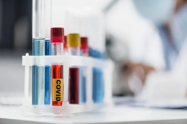 Close up of glass test tubes with covid lettering and samples with blurred background — Stock Photo