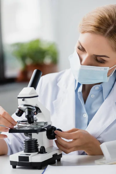 Female scientist in medical mask using microscope in lab — Stock Photo