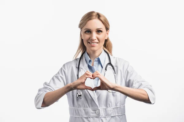 Happy nurse in white coat smiling while showing hears sign with hands isolated on white — Stock Photo