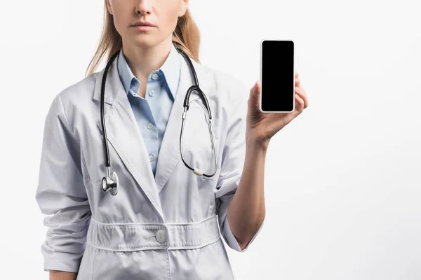 Vista recortada de la enfermera en bata blanca sosteniendo teléfono inteligente con pantalla en blanco aislado en blanco - foto de stock