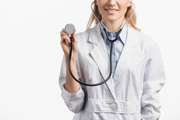 Recortado vista de feliz enfermera en blanco abrigo celebración estetoscopio aislado en blanco - foto de stock