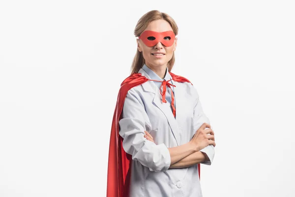 Cheerful nurse in superhero mask and cloak standing with crossed arms isolated on white — Stock Photo