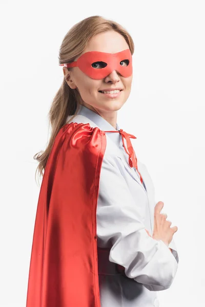 Enfermera feliz en capa de superhéroe y máscara de pie con brazos cruzados aislados en blanco - foto de stock