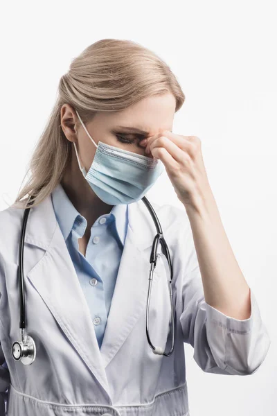 Tired nurse in medical mask and white coat suffering from headache isolated on white — Stock Photo