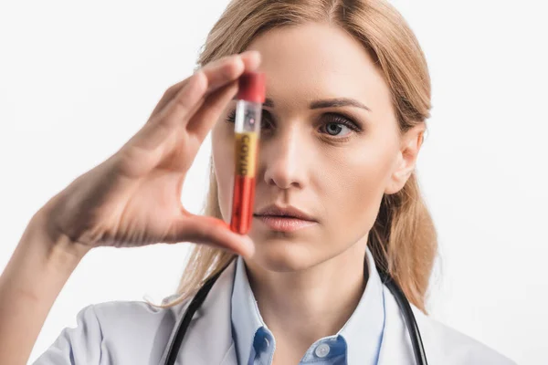 Nurse in white coat holding test tube with covid lettering on blurred foreground isolated on white — Stock Photo