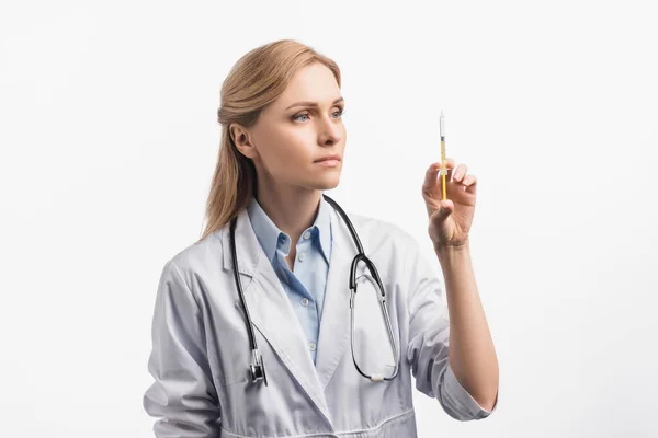 Медсестра в белом халате смотрит на шприц с вакциной, изолированной на белом — стоковое фото