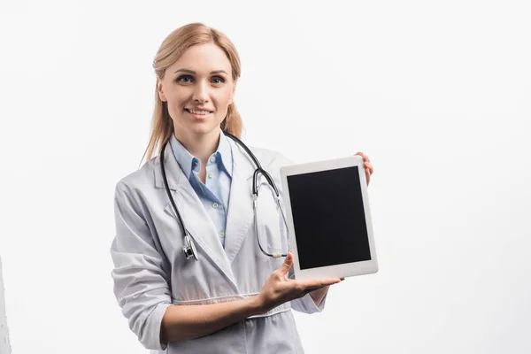 Happy nurse in white coat holding digital tablet with blank screen isolated on white — Stock Photo