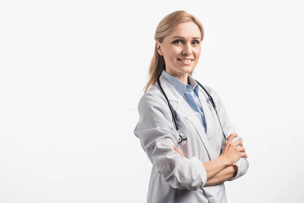 Enfermera alegre en bata blanca de pie con brazos cruzados aislados en blanco - foto de stock