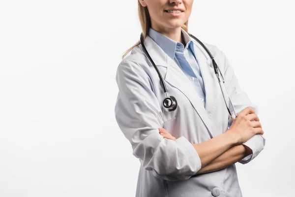 Vista recortada de alegre enfermera de capa blanca de pie con brazos cruzados aislados en blanco - foto de stock