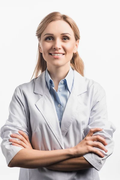 Enfermeira positiva em casaco branco em pé com braços cruzados isolados em branco — Fotografia de Stock
