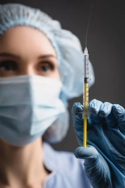 Syringe with vaccine splash in hand of nurse in latex glove on blurred background isolated on dark grey — Stock Photo