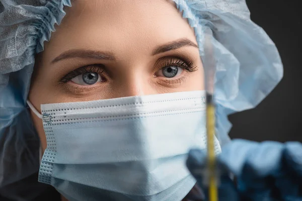 Primer plano de la enfermera en la máscara médica que sostiene la jeringa con la vacuna en primer plano borroso aislado en gris oscuro - foto de stock