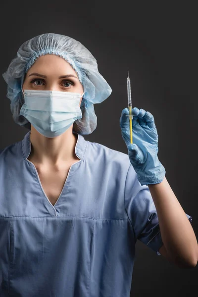 Krankenschwester in medizinischer Maske hält Spritze mit Impfstoff isoliert auf dunkelgrau — Stockfoto