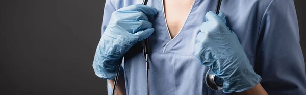 Cropped view of nurse in latex gloves adjusting stethoscope isolated on dark grey — Stock Photo
