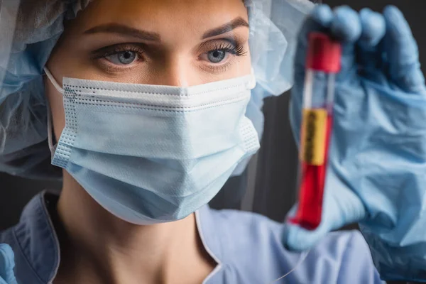 Медсестра в медицинской маске держит пробирку на размытом переднем плане, изолированном на темно-сером — стоковое фото