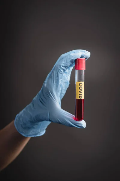 Cropped view of nurse in latex glove holding test tube with covid lettering isolated on dark grey — Stock Photo