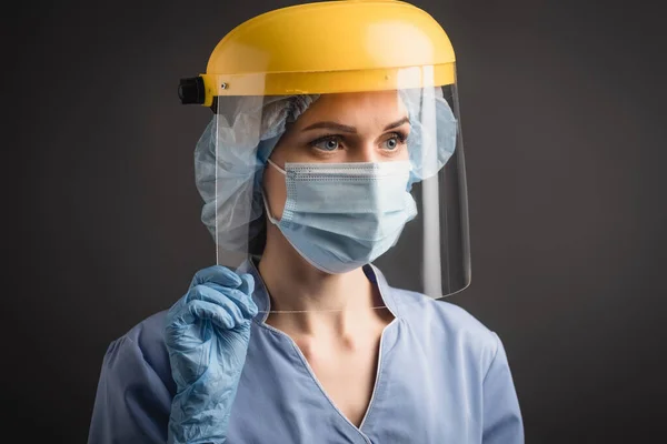 Enfermera en máscara médica, gorra y protector facial aislados en gris oscuro - foto de stock