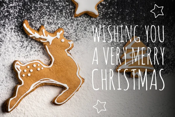Top view of cookies in shape of deer, pine and star near wishing you a very merry christmas lettering and sugar powder — Stock Photo