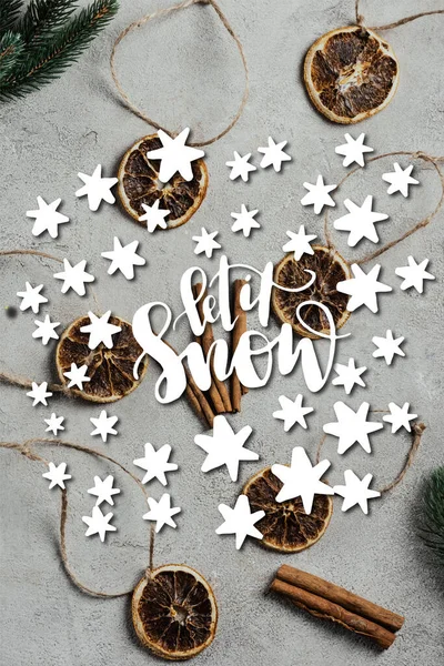 Top view of dried orange pieces with strings, cinnamon sticks and pine branches near let it snow lettering — Stock Photo