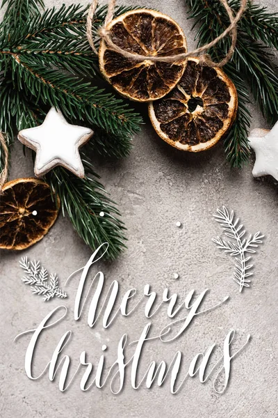Draufsicht auf getrocknete Orangenscheiben, Plätzchen und Kiefernzweig in der Nähe von frohen Weihnachten Schriftzug auf strukturiertem Hintergrund — Stockfoto