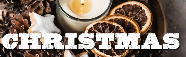 Scented candle with cookie and pine cones near christmas lettering, banner — Stock Photo