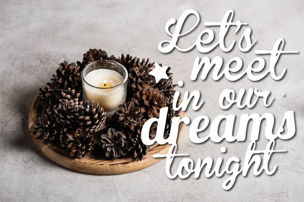 Ароматизированная свеча с сосновыми шишками на деревянной тарелке рядом давайте встретимся в наших снах сегодня вечером на сером фоне — стоковое фото