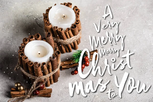 Scented candles decorated with cinnamon sticks near a very merry christmas to you lettering on textured grey background — Stock Photo