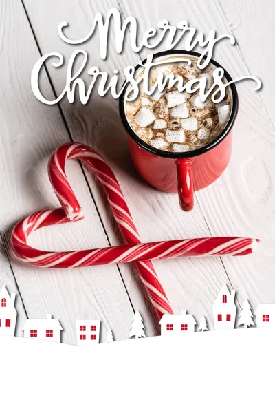 Red cup of cocoa near christmas candy canes near merry christmas lettering on wooden background — Stock Photo