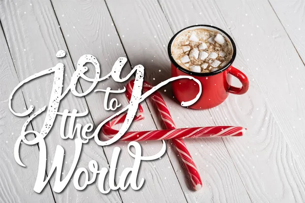 Red cup of cocoa near christmas candy canes near joy to the world lettering on wooden background — Stock Photo