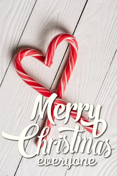 Top view of candy canes in shape of heart near merry christmas lettering on wooden background — Stock Photo