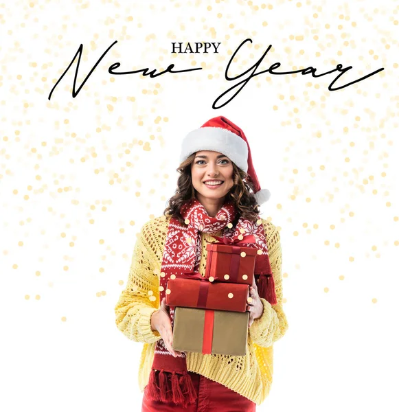 Joyful young woman in santa hat and scarf holding gifts near happy new year lettering on white — Stock Photo