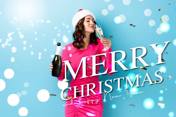 Junge Frau mit Weihnachtsmannmütze mit Flasche und Champagner in der Nähe von Konfetti und frohen Weihnachten, frohes neues Jahr Schriftzug auf blau — Stockfoto