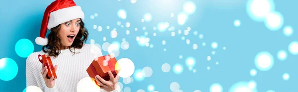 Young shocked woman looking at gift box near snow illustration on blue, banner — Stock Photo