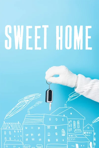 Cropped view of woman in white glove holding key near sweet home lettering and houses illustration on blue — Stock Photo